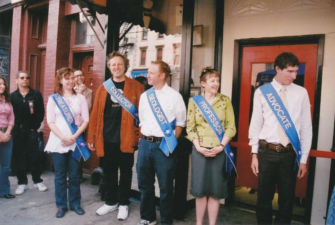 people stand in front of the Reliquary with sashes: TREASURER, COLLECTOR, GEOLOGIST, PROFESSOR, ADVOCATE