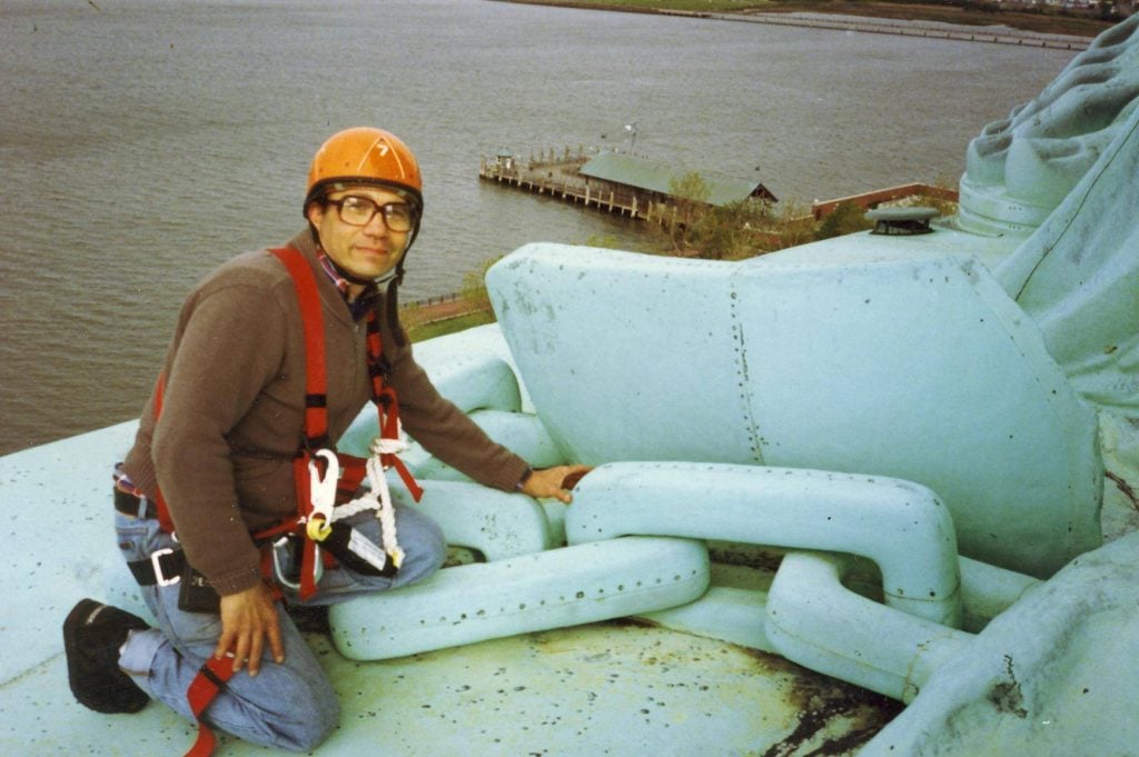 Man in hard hat next to large chain links the size of himself on the Statue of Liberty