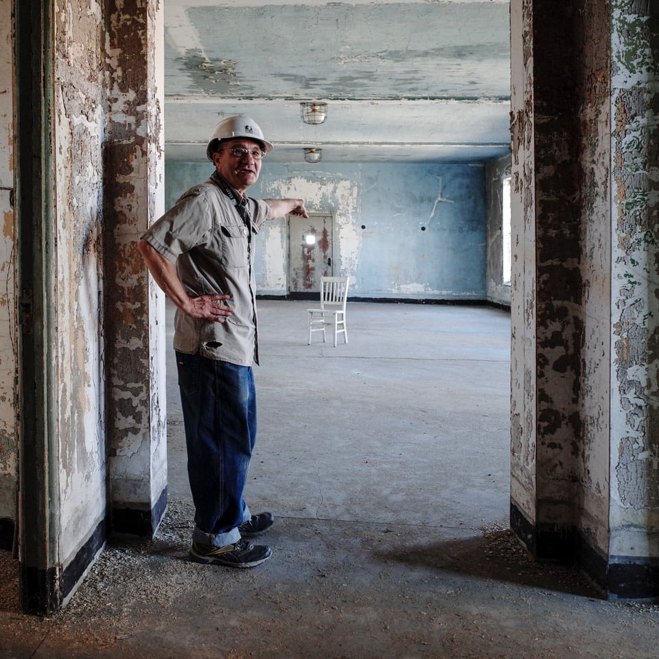 Man in hard hat stand in doorframe in front of an empty room with a single chair
