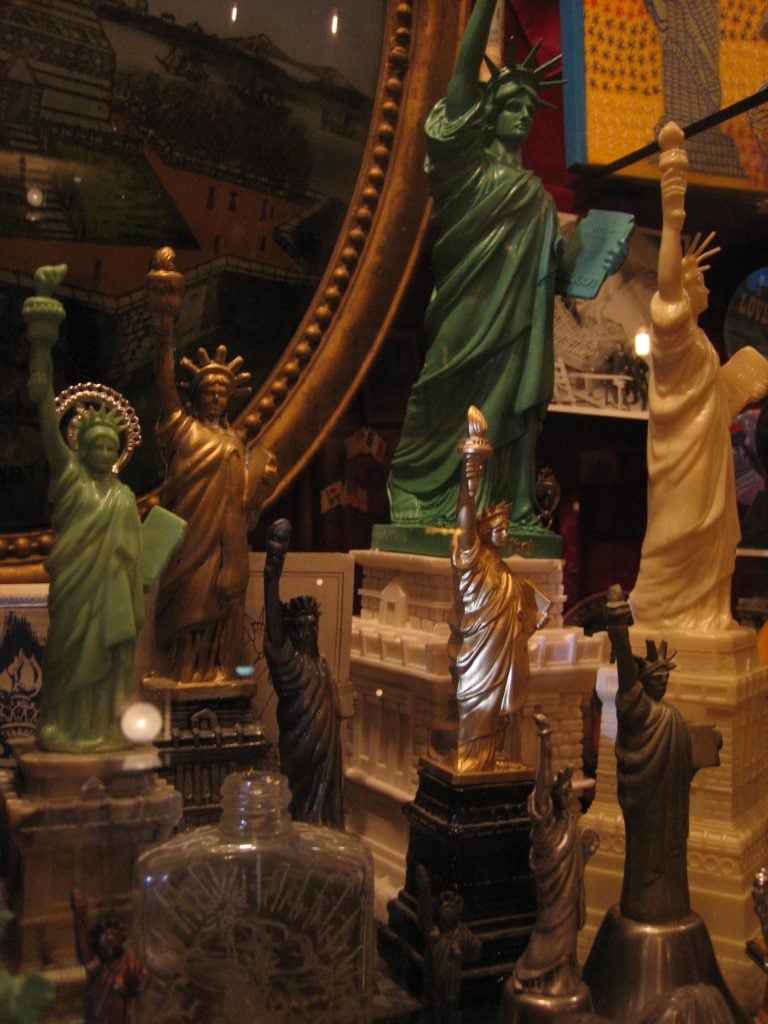 Closeup of more Statue of Liberty figurines from the Reliquary collection. Some are metal, others plastic. Some green, some white, some metallic.