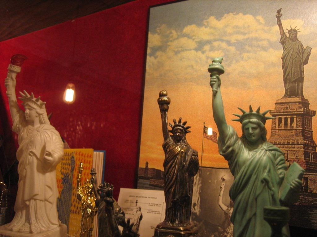 Close-up of 5 statues in the vitrine of hundreds of Statues of Liberty figurines in the City Reliquary
